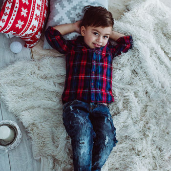 uśmiechnięty chłopiec leżący na futrzanym dywanie wśród bożonarodzeniowych dekoracji